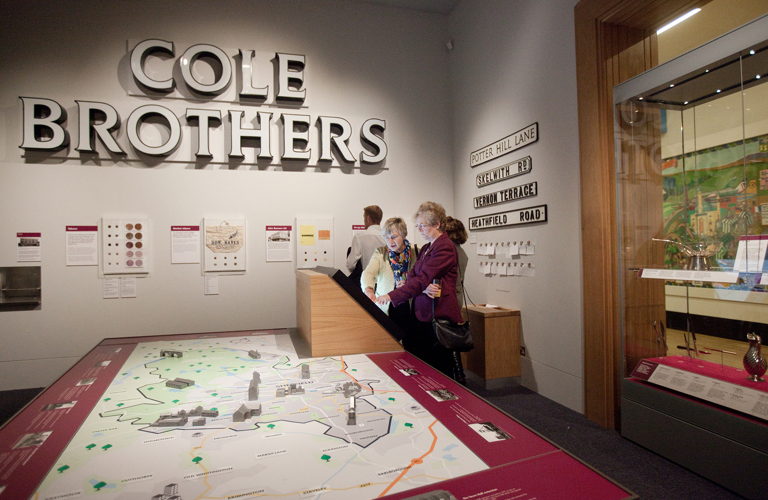 A large sign above a map, with four adults looking at images on a wall and an interactive screen 