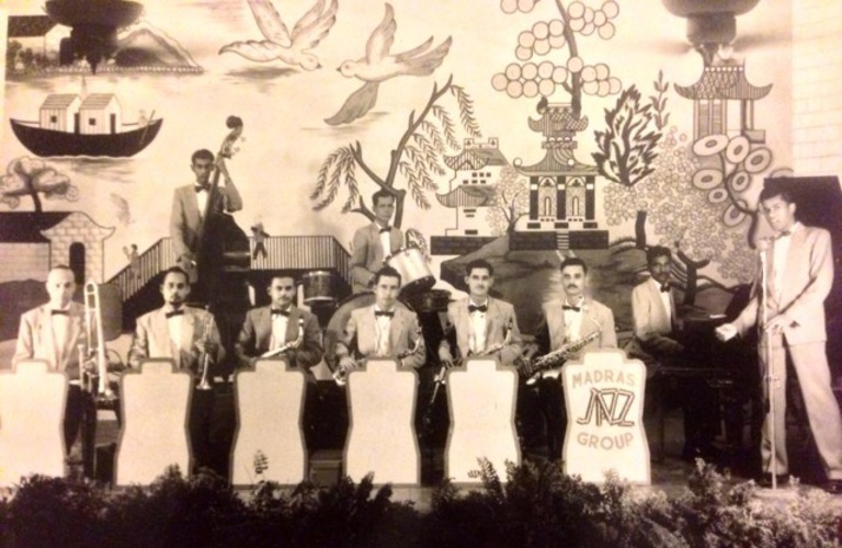 A black and white photograph of a group of people in formal dress playing musical instruments. 