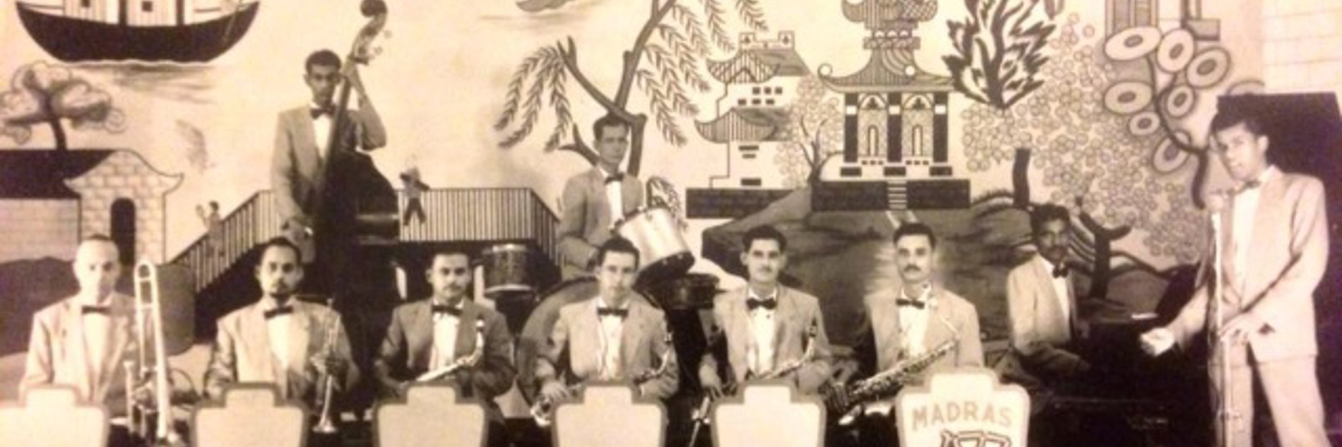 A black and white photograph of a group of people in formal dress playing musical instruments. 