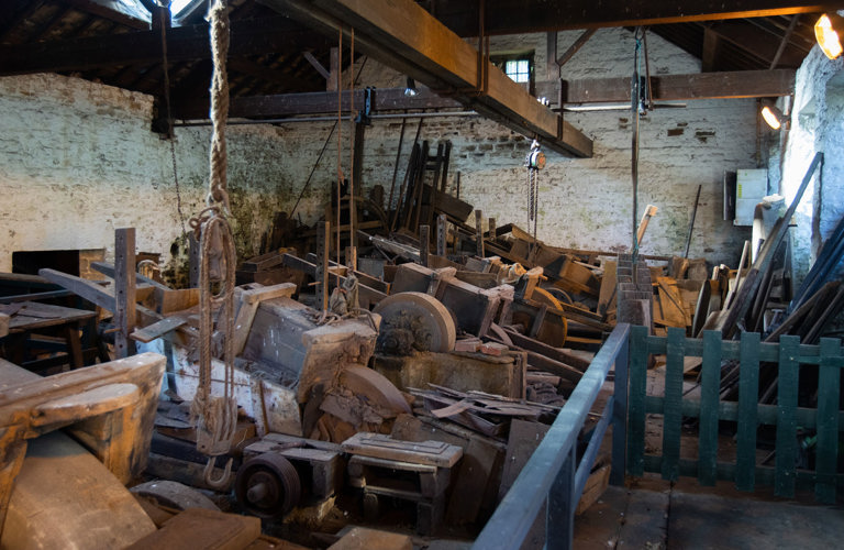 Old whitewashed workshop with exposed wooden roof beams and a row of grinding wheels with ‘saddles’.