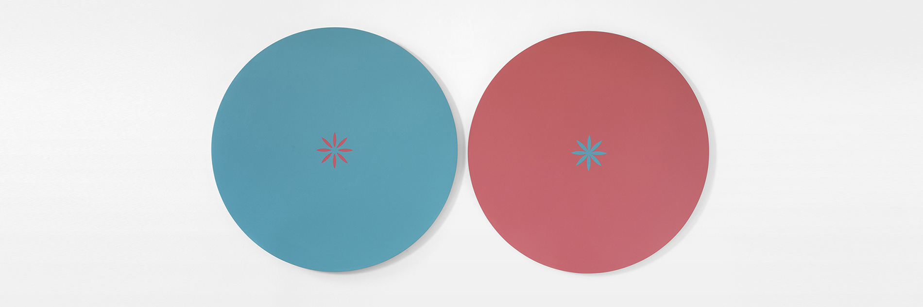 A painting of two coloured circles side by side on a white background. The left circle is blue, with a small pink star at its centre.  The right circle is pink, with a small blue star at its centre.  