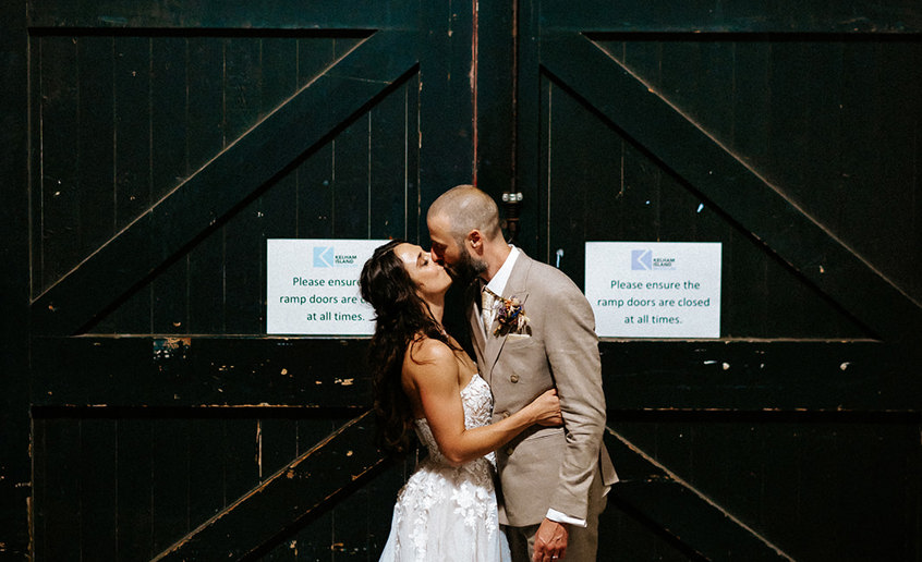 Bride and groom kissing in front of a large, old, wooden door painted black.