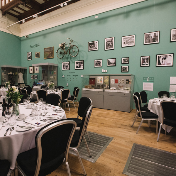 A gallery with tables set for a wedding dinner. Objects and framed photographs cover teh walls. 