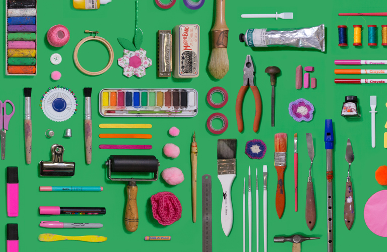 A selection of different crafting utensils (ink rollers, pliers, paint brushes etc) arranged on a green background.