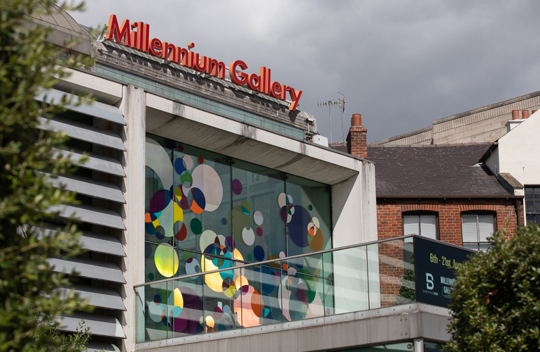 The external, upper glass door and windows of the Millennium Gallery which has multiple, multicoloured shaped dots in red, blue, yellow, green and blue on them