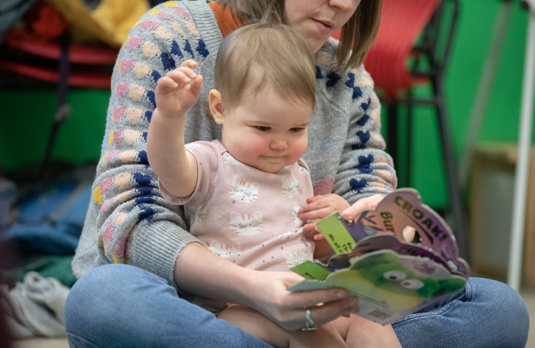 A photograph of a baby and an adult reading a book. 