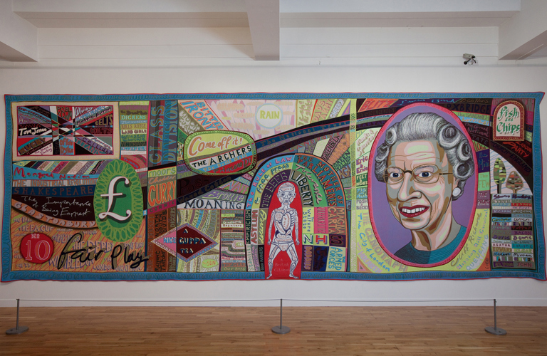 A multi-coloured tapestry in a long landscape format incorporating a huge variety of text and images on the theme of ‘Britishness’. An image of Queen Elizabeth II and the pound symbol feature prominently.			
