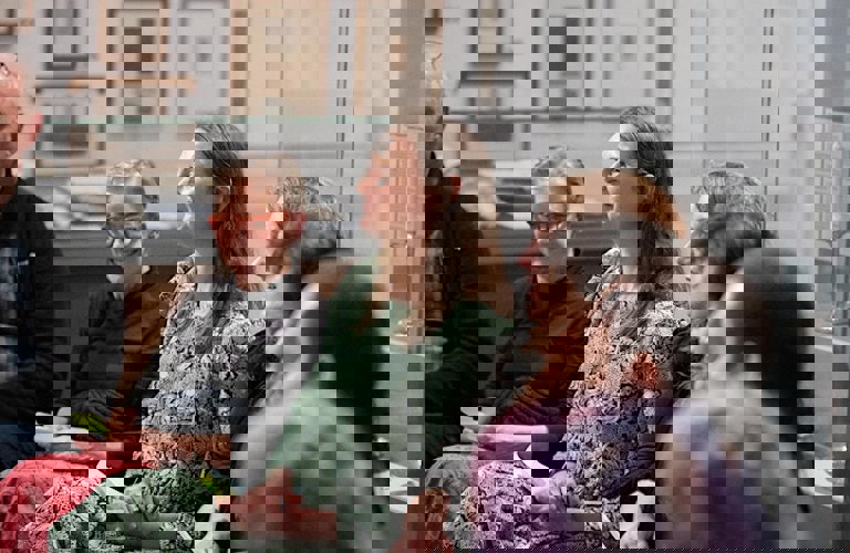 A group of seven people sat in a curved row in a gallery space, with framed images visible on the walls behind them. People are smiling and look happy