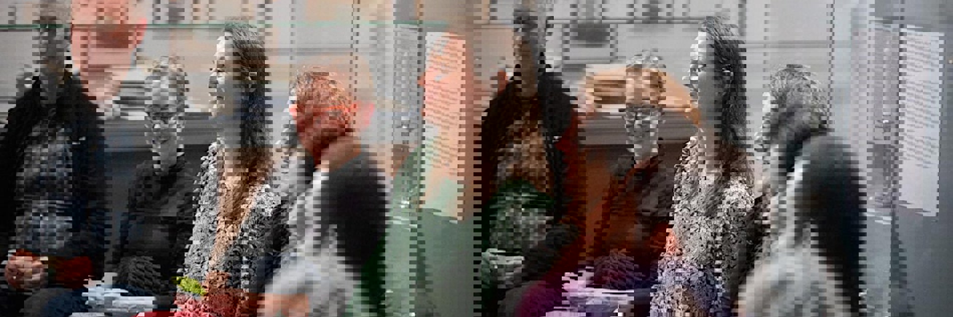 A group of seven people sat in a curved row in a gallery space, with framed images visible on the walls behind them. People are smiling and look happy