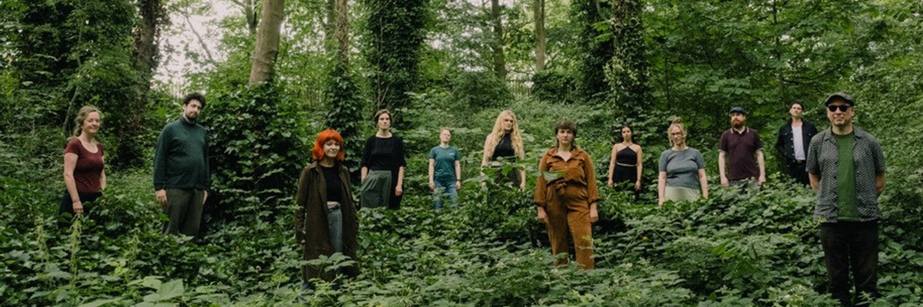 A photograph of twelve people stood in a forest, with the trees towering above them