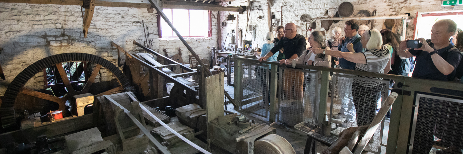 A group of adults looking at historical machinery in a grinding workshop. 