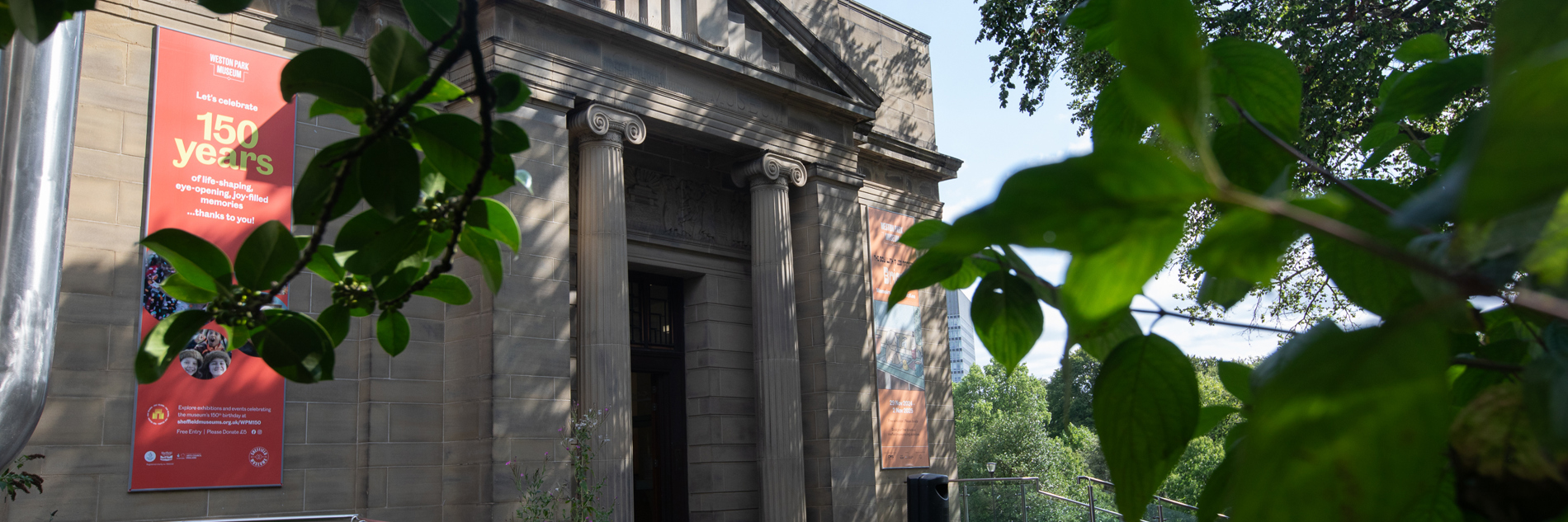 A photograph of the entrance to Weston Park Museum, with leaves obscuring the view in the foreground.