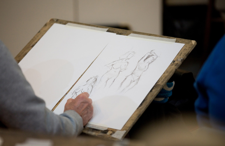 A photograph of an outline of an adult's arm and hand sketching several life drawing poses.  