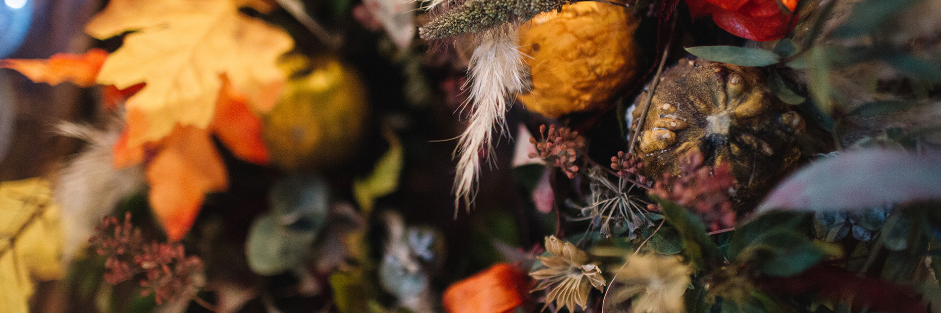 A close-up of an autumnal bouquet made up of foliage and flowers in greens, yellows, oranges, purples and blues