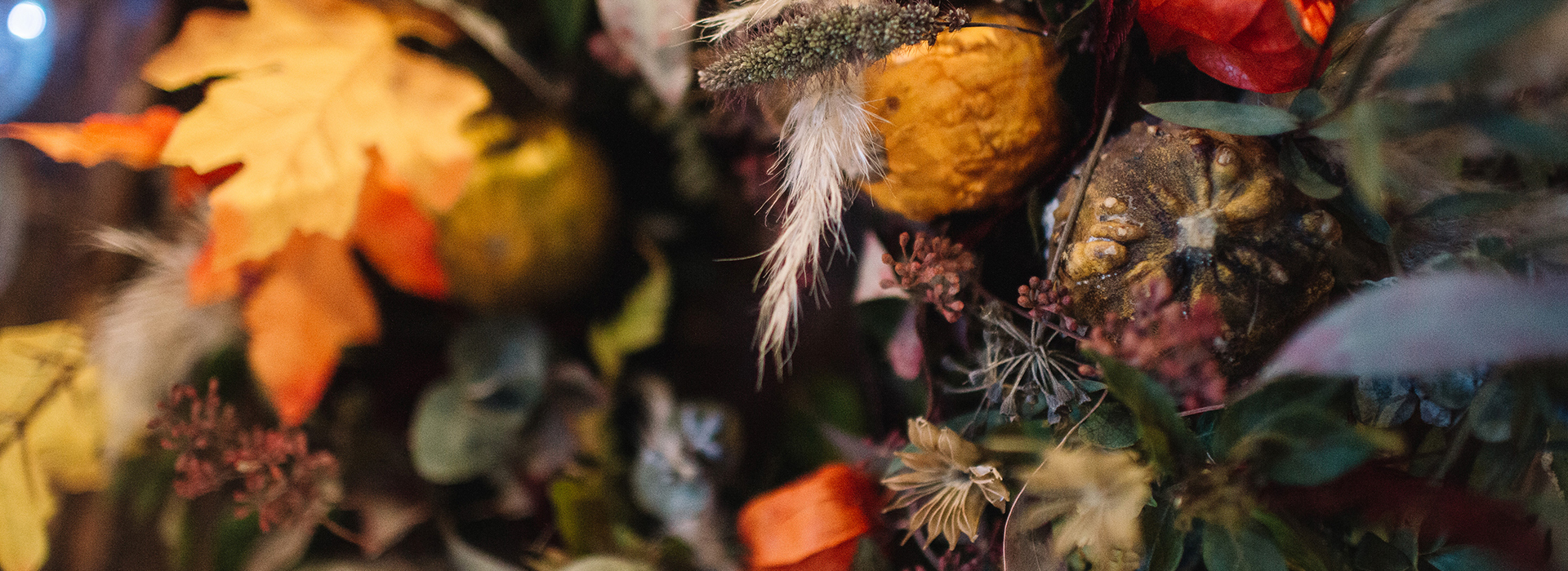 A close-up of an autumnal bouquet made up of foliage and flowers in greens, yellows, oranges, purples and blues