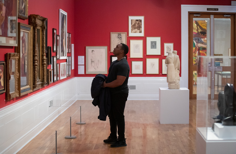 A visitor stands in Graves Gallery, looking at artworks on the red walls. 