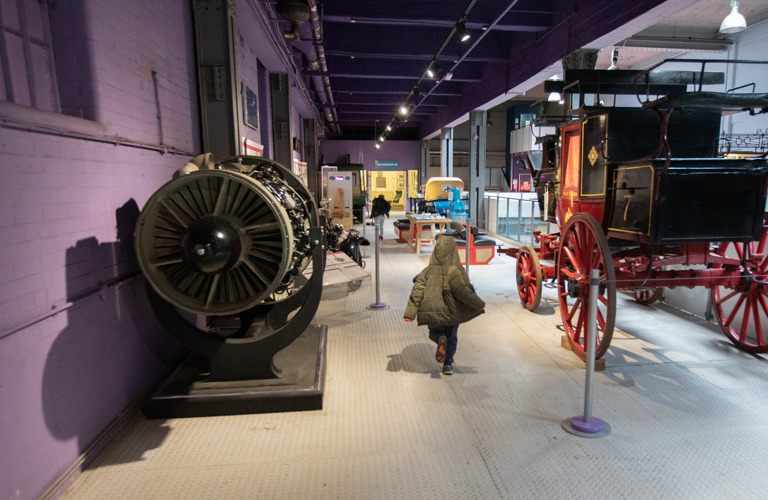 A view of the gallery showing the backs of two children, a black and red trailer and the side of an engine. 