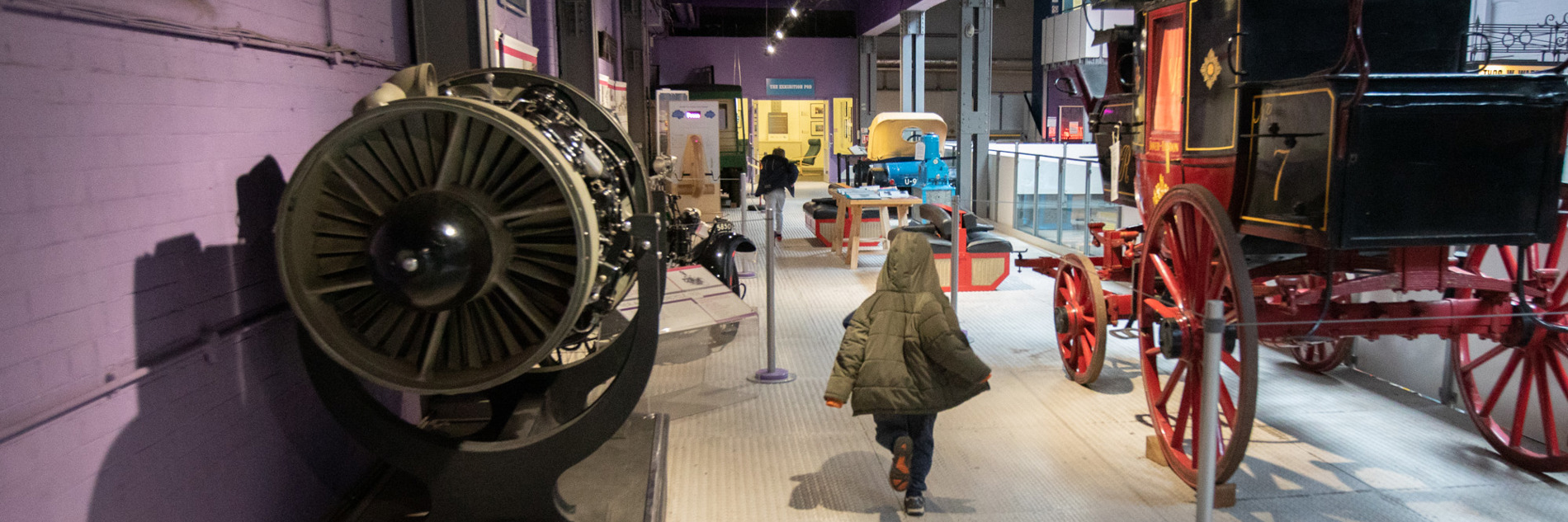 A view of the gallery showing the backs of two children, a black and red trailer and the side of an engine. 