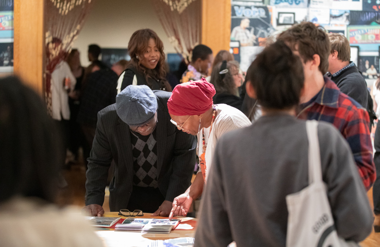 Two older adults looking down at an unseen object in front of a group of adults. 