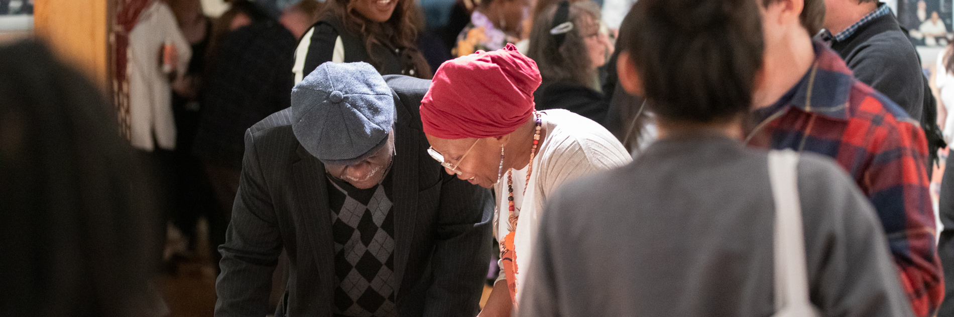 Two older adults looking down at an unseen object in front of a group of adults. 