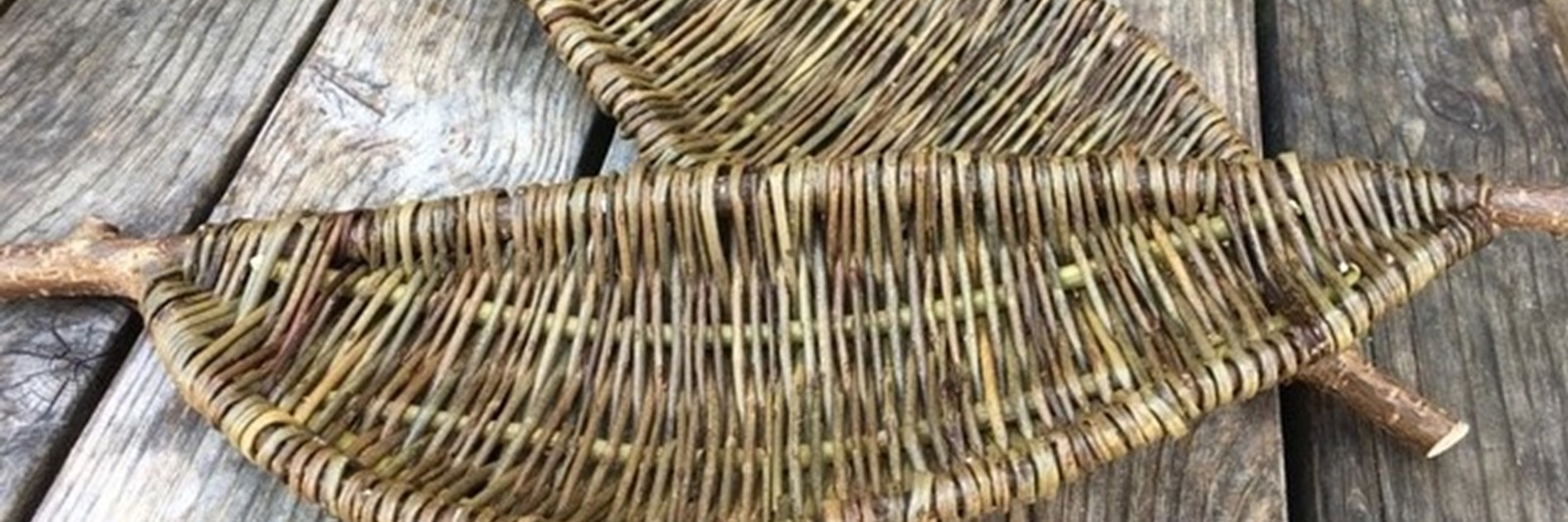 A photograph of two handwoven leaf shaped willow panels. They are placed on wooden slats.