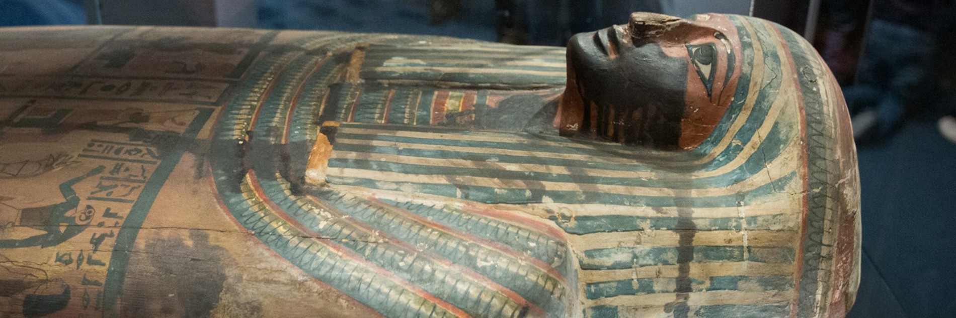 A photograph of the mummy in Weston Park Museum. The sarcophagus is decorated with blue and orange lines, with bold black lines around the eyes and mouth.