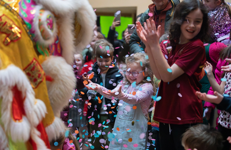 A photograph of children celebrating at Weston Park Museum. They are smiling with their hands stretched in front of them, while confetti falls in the air before them.