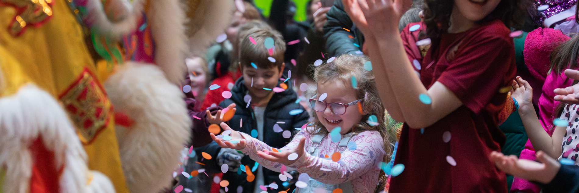 A photograph of children celebrating at Weston Park Museum. They are smiling with their hands stretched in front of them, while confetti falls in the air before them.