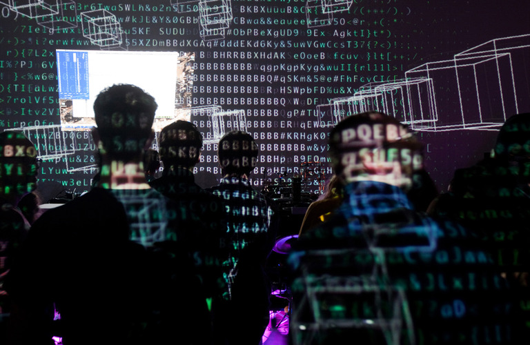 A group of seated adults watching a projection with symbols and shapes projected on their backs and on the surface in front of them