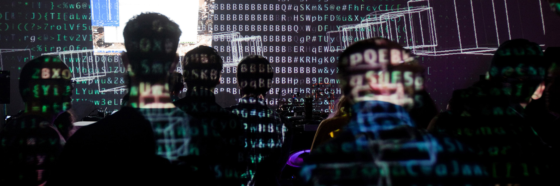 A group of seated adults watching a projection with symbols and shapes projected on their backs and on the surface in front of them