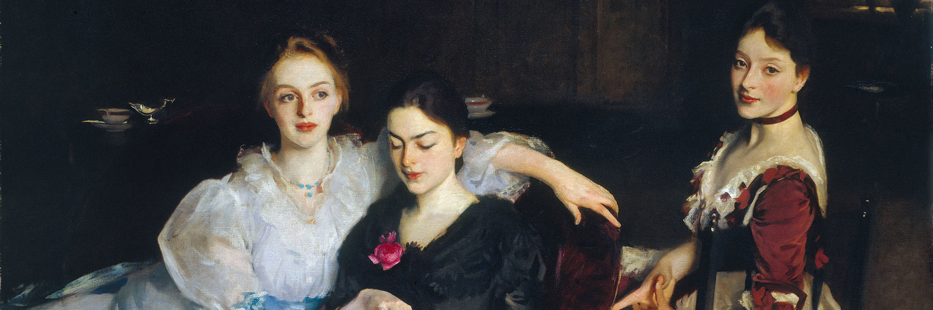 An oil painting of three women in formal Victorian dress. They are sitting informally next to each other - two women are sharing a chair and looking at a book, and the third woman is sitting on a chair behind them. The painting has a dark background, with the outline of a dresser on which sits a silver jug and a porcelain bowl. 