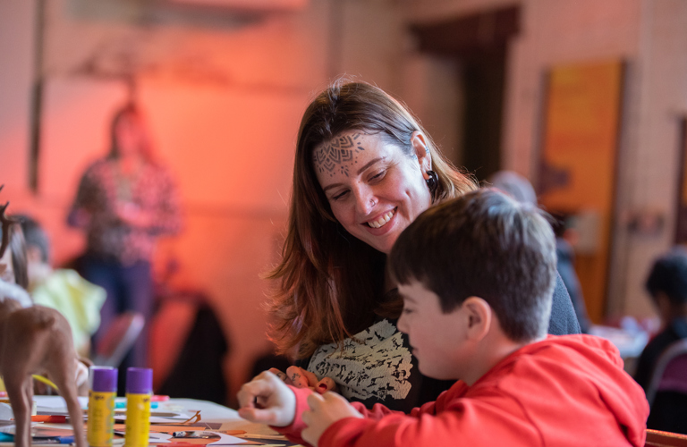 Carer smiling at her child who is sitting next to her making something.