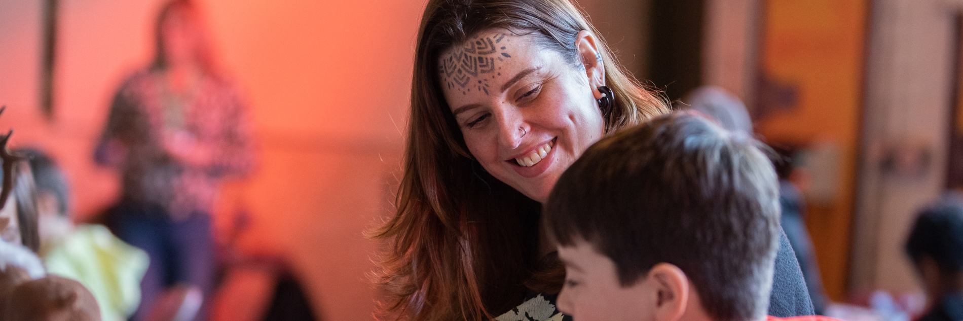 Carer smiling at her child who is sitting next to her making something.