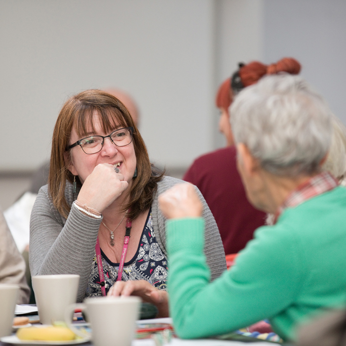 A group of adults talking, the one facing the camera is smiling. 