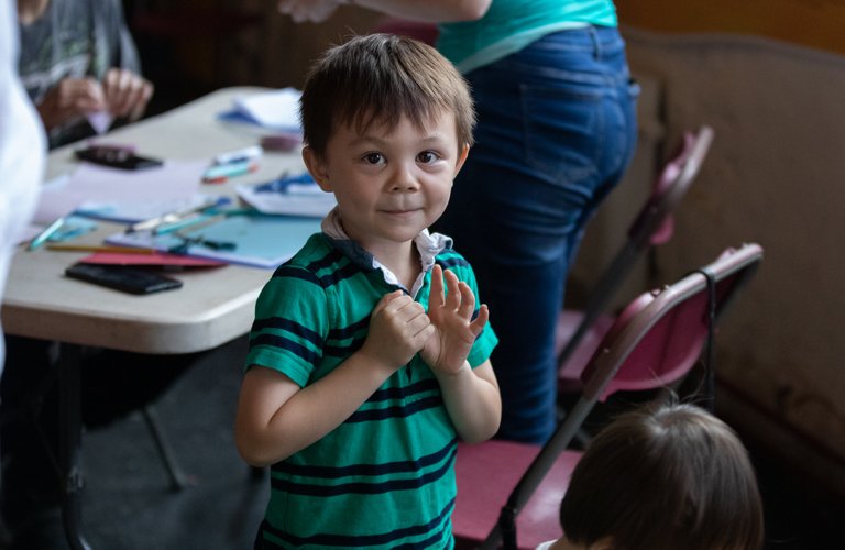 A photograph of a young boy waving at the camera.