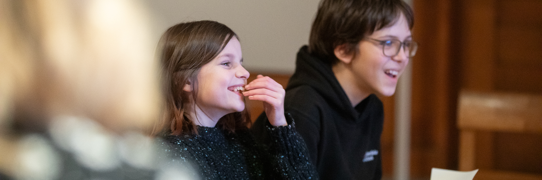 A photograph of two smiling children sitting on a wooden bench in an art gallery. 