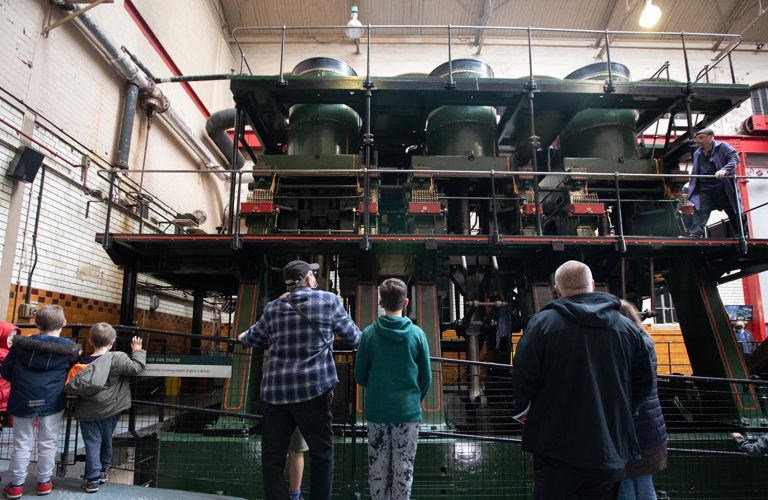 A small group of adults and children viewed from behind, looking up at the River Don Steam Engine.