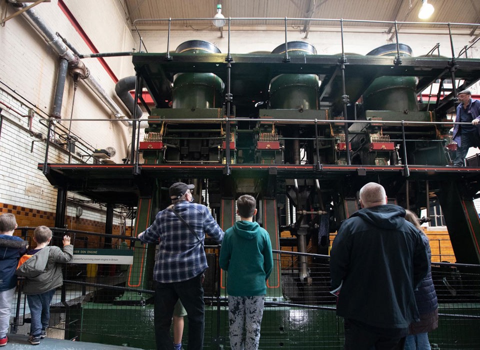 A small group of adults and children viewed from behind, looking up at the River Don Steam Engine.